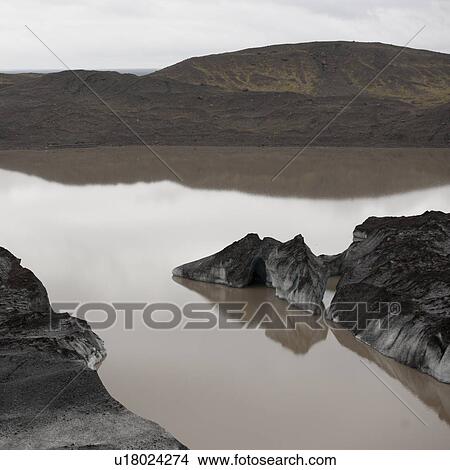 Picture - Muddy iceberg in reflective glacial lake and coastline. Fotosearch