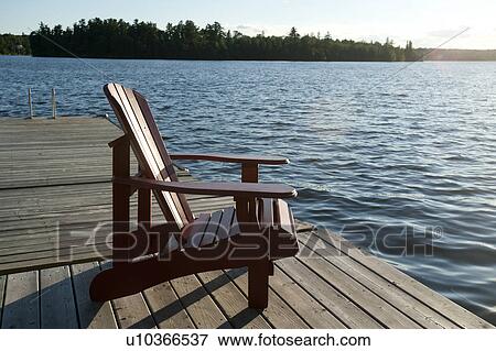 Stock Photo - Muskoka chair on the dock overlooking the lake at Lake of the Woods, Ontario. Fotosearch