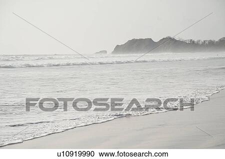 Stock Image - Overcast day at the seaside with waves lapping up against the sandy beach. Fotosearch