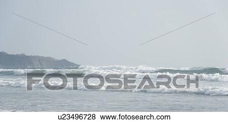 Stock Photo - Overcast day at the seaside with waves lapping up against the sandy beach. Fotosearch