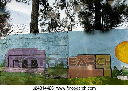 Stock Image - Painting of houses and buildings on concrete cinderblock wall, with barbed wire . Fotosearch