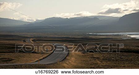 Stock Photograph - Paved highway meandering through dry farmland towards misty mountains. Fotosearch