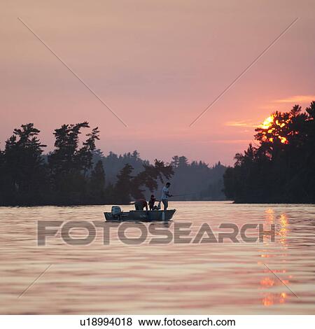 Stock Photo - People in a boat at sunset in Lake of the Woods, Ontario. Fotosearch