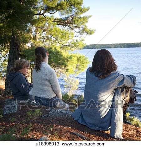 Stock Image - People sitting at the shoreline in Lake of the Woods, Ontario. Fotosearch