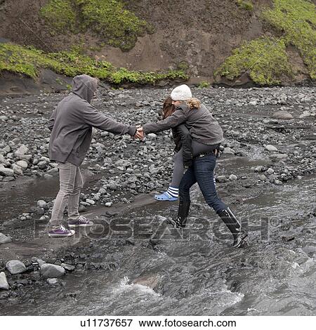 Stock Photo - People walking through a stream to a rocky riverside canyon. Fotosearch