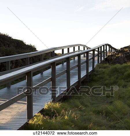 Stock Image - Railed boardwalk over grassy hill. Fotosearch