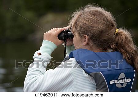 Stock Image - Rear view of a girl wearing a life jacket looking through binoculars at Lake of the Woods, Ontario . Fotosearch