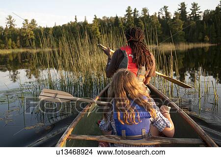 Rear view of blond girl and Africian American man rowing in a canoe at Lake of the Woods, Ontario View Large Photo Image Picture - Rear view of blond girl and Africian American man rowing in a canoe at Lake of the Woods, Ontario. Fotosearch