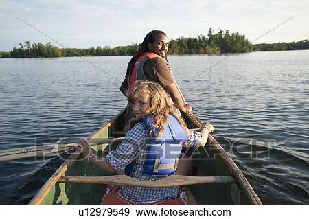 Stock Photo - Rear view of blond girl and Africian American man rowing in a canoe at Lake of the Woods, Ontario. Fotosearch