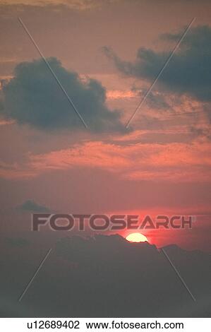 Stock Image - Red evening sunset over the ocean hidden behind the clouds. Fotosearch