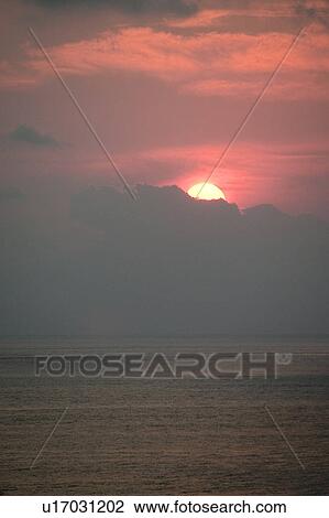 Stock Image - Red evening sunset over the ocean hidden behind the clouds. Fotosearch