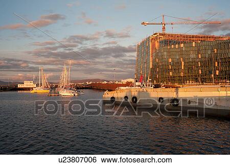 Stock Photograph - Reykjavik harbour wharf and ships, Conference Centre building site, reflections of the evening in the ocean water. Fotosearch