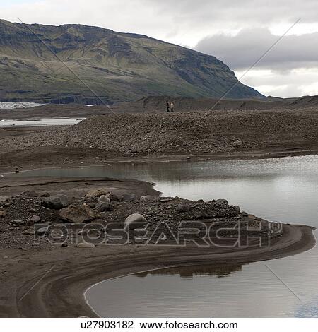 Stock Image - Rocky shore of glacial lake before distant mountains. Fotosearch