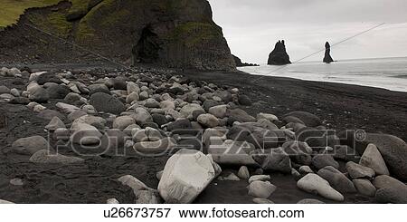 Stock Photo - Rocky shoreline with cave, black volcanic sand, stacks offshore. Fotosearch