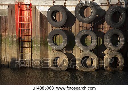 Stock Image - Rubber tire lined wharf with fluourescent access ladders. Fotosearch