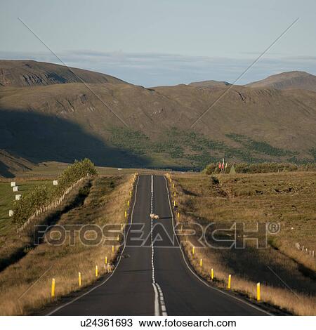 Stock Image - Rural farmland asphalt highway disappearing into countryside toward mountain. Fotosearch