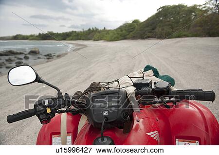 Sandy beach with encroaching trees, with rocks in the surf, on an overcast cloudy day fand the handlebars of a red Quad bike with a rear view mirror View Large Photo Image Stock Photo - Sandy beach with encroaching trees, with rocks in the surf, on an overcast cloudy day fand the handlebars of a red Quad bike with a rear view mirror. Fotosearch
