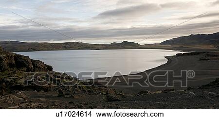 Picture - Serene lake with volcanic black sand and rocky hill. Fotosearch