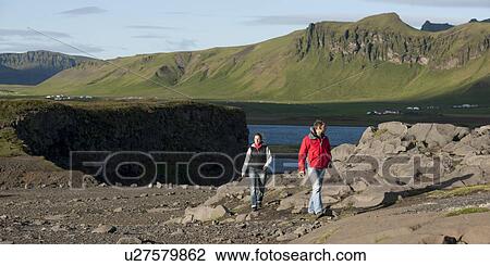 Stock Image - Sightseers walking away from scenic vista of mountains and waterbody, and cliffs. Fotosearch