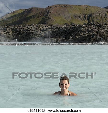 Stock Image - Smiling woman in bathing suit submerged in geothermal mineral pool. Fotosearch