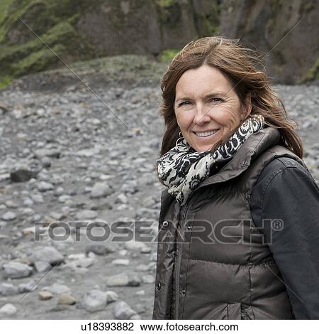 Stock Image - Smiling woman in scarf and vest at rocky dry riverbed before cliff. Fotosearch
