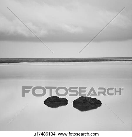 Picture - Solitary rocks in calm lake under cloudy sky near shore. Fotosearch