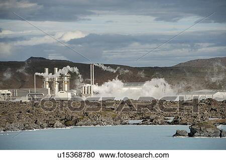 Stock Image - Steam rising from a geothermal power station above a rocky lake coastline. Fotosearch