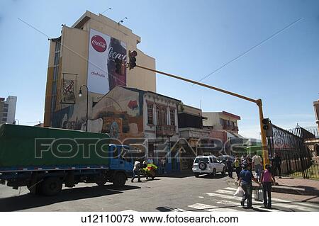 Stock Image - Streetscape in San Jose, livery truck passing under a traffic light, passing by a Coca Cola advertisement, with murals painted on the two storey building. Fotosearch
