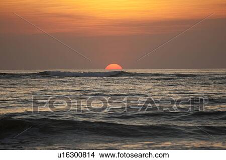 Sun setting over the calm ocean with an orange glow View Large Photo Image Picture - Sun setting over the calm ocean with an orange glow. Fotosearch