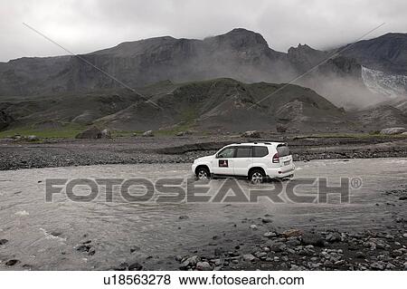 Stock Photo - SUV driving across a shallow river belowa misty mountain range. Fotosearch