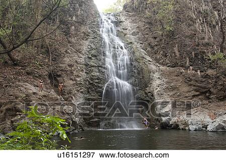 Stock Photo - Swimmers in a secluded lagoon under a waterfall cascading over a steep rock face. Fotosearch