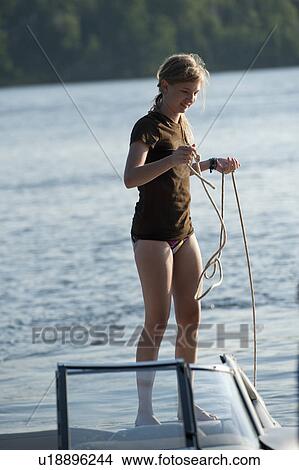 Picture - Teenage girl holding a rope while standing on a boat in Lake of the Woods, Ontario. Fotosearch