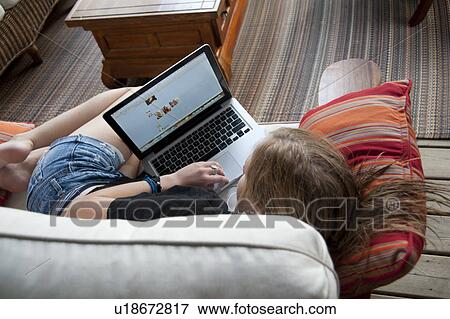 Teenage girl relaxing on a sofa while looking at a laptop computer View Large Photo Image Stock Photo - Teenage girl relaxing on a sofa while looking at a laptop computer. Fotosearch