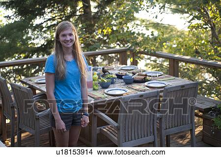 Picture - Teenage girl standing by patio dining table on a deck. Fotosearch