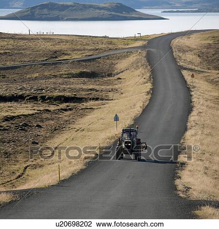 Stock Image - Tractor on rural highway through countryside towards coastline and islands. Fotosearch