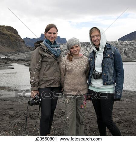 Stock Image - Trio of girls standing in front of glacier and lakeshore. Fotosearch