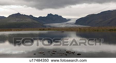 Stock Image - Vatnajokull glacier, mountains, and clouds reflected in water along coastline. Fotosearch