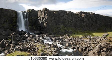 Stock Image - Waterfall cascading from cliff to rock bed. Fotosearch
