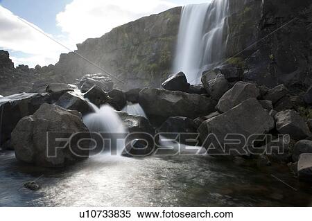 Waterfall cascading onto boulders into a river View Large Photo Image Stock Photography - Waterfall cascading onto boulders into a river. Fotosearch