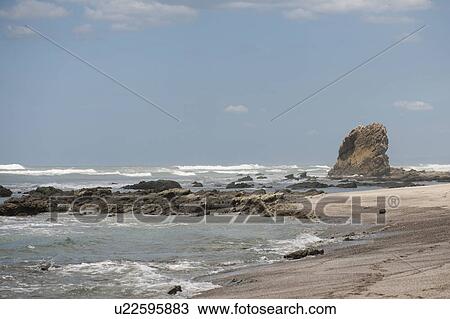 Stock Image - Waves lapping up against a sandy beach with an outcropping of rocks, and a stack in the background. Fotosearch