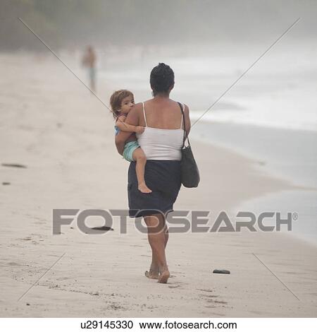 Stock Image - Woman carrying a child on the shoreline in Costa Rica. Fotosearch