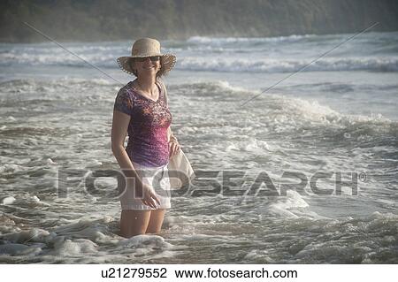 Woman in a hat smiling standing in the ocean surf at knee height View Large Photo Image Stock Image - Woman in a hat smiling standing in the ocean surf at knee height. Fotosearch