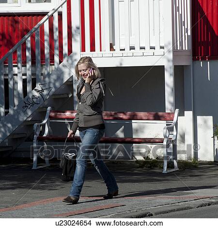 Picture - Woman in casual clothing walking on sidewalk talking on cell phone. Fotosearch
