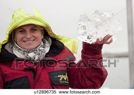 Stock Photography - Woman in red parka and yellow hood holding clear ice chunk. Fotosearch