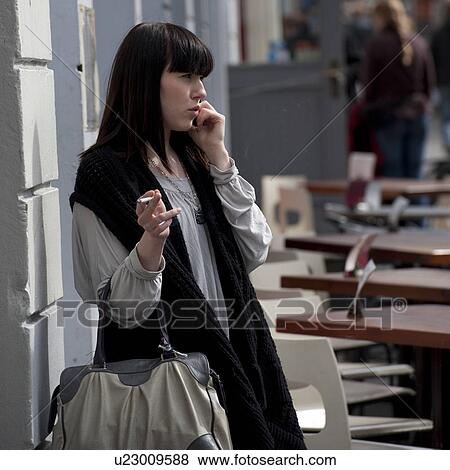 Woman outside talking on a cell phone, smoking and holding a purse View Large Photo Image Stock Photo - Woman outside talking on a cell phone, smoking and holding a purse. Fotosearch