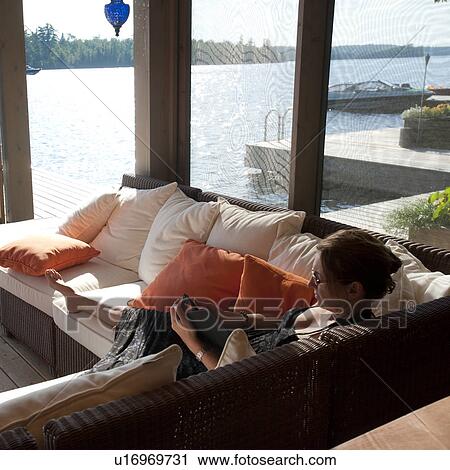 Woman sitting on a sofa looking at her cell phone at Lake of the Woods, Ontario View Large Photo Image Stock Image - Woman sitting on a sofa looking at her cell phone at Lake of the Woods, Ontario. Fotosearch