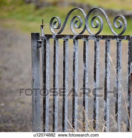 Stock Image - Wrought iron gate on rural lane. Fotosearch