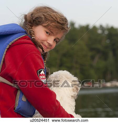 Stock Image - Young girl wearing a life jacket with her dog in Lake of the Woods, Ontario. Fotosearch