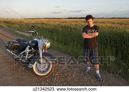 Young man standing by the roadway with a motorcycle View Large Photo Image Stock Image - Young man standing by the roadway with a motorcycle. Fotosearch