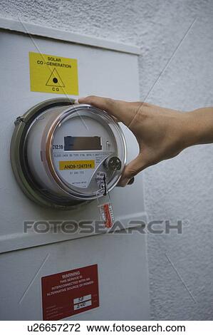 Stock Image - Hand on meter of solar generation unit in Los Angeles, California. Fotosearch